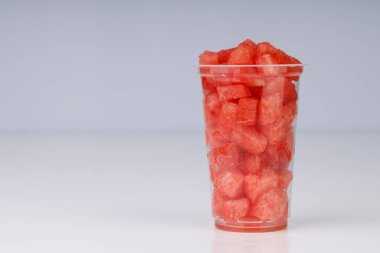 Karpuz dilimleri, beyaz arka planda şeffaf bir bardakta dizilmiş, izole edilmiş.