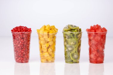 Karpuz, ananas, nar ve kivi dilimleri iki şeffaf bardakta, beyaz arka planda, izole edilmiş.