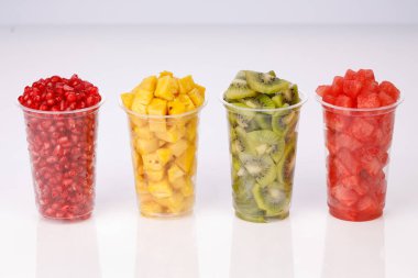 Karpuz, ananas, nar ve kivi dilimleri iki şeffaf bardakta, beyaz arka planda, izole edilmiş.