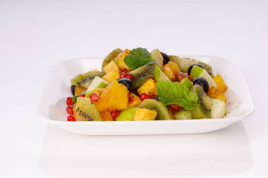 Karışık meyve salatası beyaz bir sofra takımına dizilmiş ve nane yaprağıyla süslenmiş..