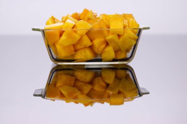 Olgun mango küpleri ya da beyaz arkaplan ile cam kare bir kapta düzenlenmiş parça.