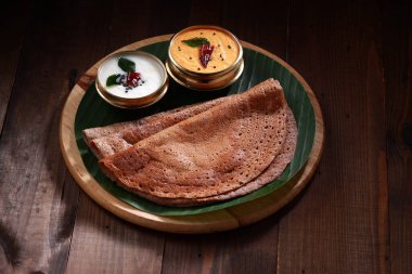 Ragi Dosa, yanında muz yaprağı ve hindistan cevizi turşusuyla kaplı yuvarlak ahşap bir zemine yerleştirilmiş sağlıklı bir Güney Hindistan kahvaltısı..