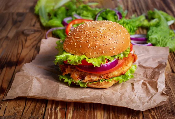 Tahta bir masada etli, soğanlı ve yeşil salatalı hamburger.