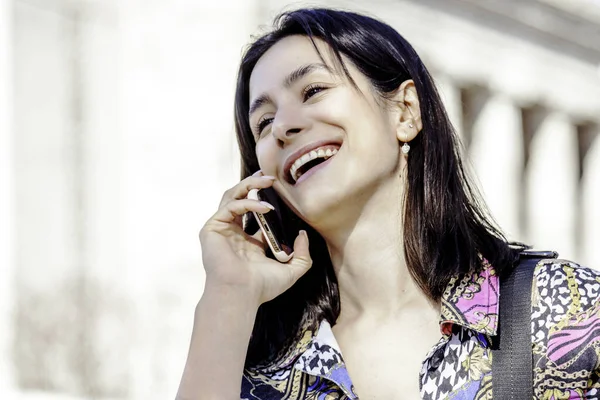 Genç bir kadın sokakta cep telefonuyla konuşuyor ve gülümsüyor.