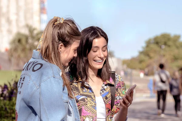 Kadınlar sokakta cep telefonu kullanır ve gülerler.