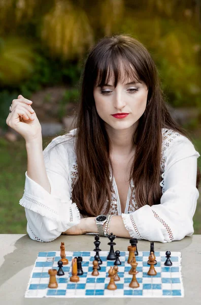 Young woman playing chess thinking about her move, outdoors.