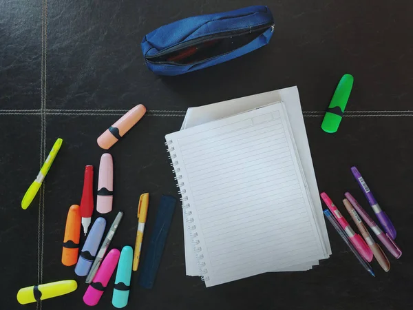 Çizgili defter, renk kalemleri ve kalem kutusu olan bir masada ders çalış