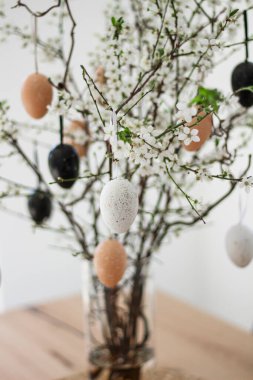 Ahşap bir masadaki vazoda paskalya renkli yumurtalarla süslenmiş taze dallar. Tatil konsepti, ev dekorasyonu, mutlu çocukluk ve aile gelenekleri..