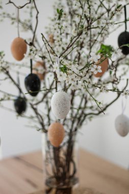 Ahşap bir masadaki vazoda paskalya renkli yumurtalarla süslenmiş taze dallar..