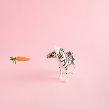 Zebra ve havuç pastel pembe arka planda. Plastik oyuncaklardan yapılmış en az yaratıcı konsept.