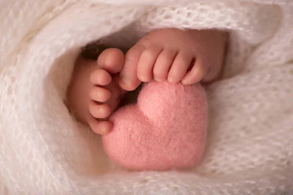 Piernas y dedos de los pies de un recién nacido en una manta blanca suave con un corazón rosado — Foto de Stock