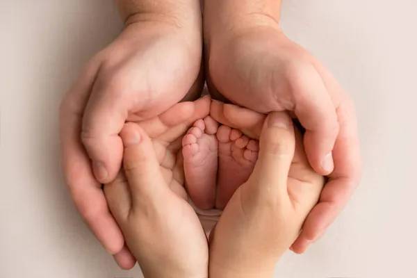 Ben, tår, fötter och hälar från en nyfödd. Med händerna på föräldrar, far, håller mor försiktigt barnbenen. Makrofotografi, närbild. — Stockfoto