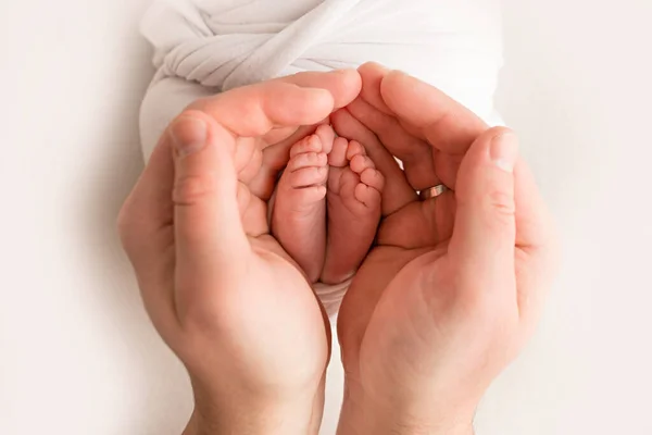 Pernas, dedos dos pés, pés e saltos de um recém-nascido. Com as mãos dos pais, pai, a mãe segura suavemente as pernas das crianças. Fotografia macro, close-up. — Fotografia de Stock