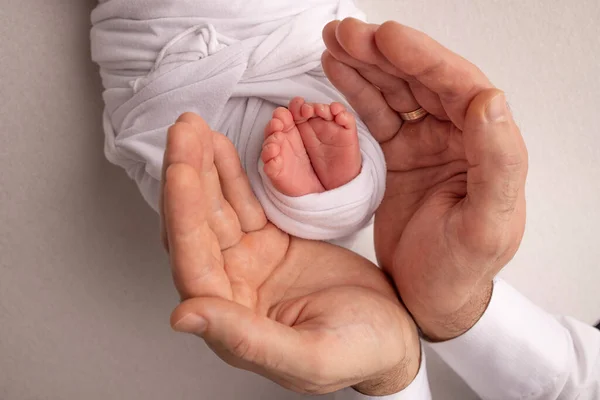 Dłonie ojca, matka trzymają stopę nowonarodzonego dziecka w białym kocu. Stopy noworodka na dłoniach rodziców. Studio fotografia dzieci palce, szpilki i stopy. — Zdjęcie stockowe