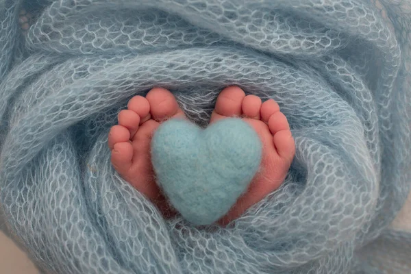 De kleine voet van een pasgeboren baby. Zachte voeten van een pasgeborene in een blauwe deken. Close-up van tenen, hakken en voeten van een pasgeborene. Gebreid blauw hart in de benen van een baby. Studiofotografie. — Stockfoto