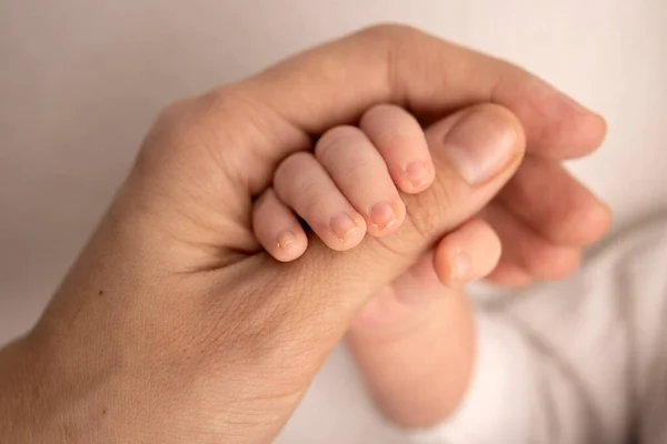 El bebé recién nacido en un blanco se cierra tiene un agarre firme en el dedo de los padres después del nacimiento. Primer plano de la pequeña mano del niño y la palma de la madre y el padre. Concepto de crianza, cuidado de niños y atención médica. — Foto de Stock