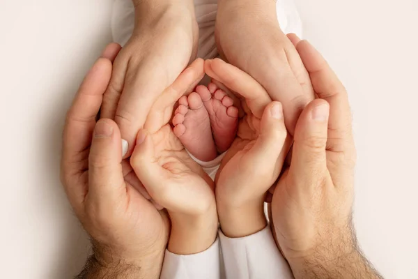 As palmas das mãos do pai, a mãe está segurando o pé do bebê recém-nascido. Pés do recém-nascido nas palmas das mãos dos pais. Fotografia de estúdio de umas crianças dedos do pé, saltos altos e pés. — Fotografia de Stock