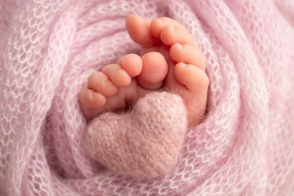 El pequeño pie de un bebé recién nacido. Pies suaves de un recién nacido en una manta rosa. Primer plano de los dedos de los pies, tacones y pies de un recién nacido. Corazón rosa de punto en las piernas de un bebé. Estudio macro fotografía. —  Fotos de Stock