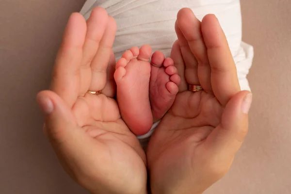 Annenin, babanın avuç içleri yeni doğan bebeğin ayağını beyaz bir battaniyenin içinde tutuyor. Yeni doğan bebeğin ayakları, ebeveynlerin avuçlarında. Stüdyo fotoğrafçılığı. Ayak, ayak ve ayak parmakları.. — Stok fotoğraf