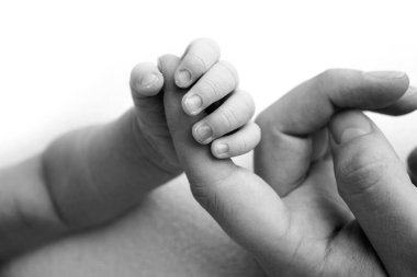 Yeni doğan bebek, doğumdan sonra ebeveyn parmağına sıkı sıkıya tutunur. Çocuğun küçük eli ve anne ve babanın avuç içi. Ebeveynlik, çocuk bakımı ve sağlık hizmeti konsepti. Siyah beyaz fotoğraf.