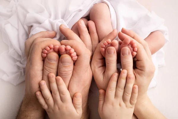 Pieds de jumeaux nouveau-nés. Deux paires de pieds de bébé. Les parents, le père, la mère et le frère aîné, la sœur tiennent les jumeaux par les jambes. Gros plan - orteils, talons et pieds d'un nouveau-né. Frères nouveau-nés, sœurs. — Photo