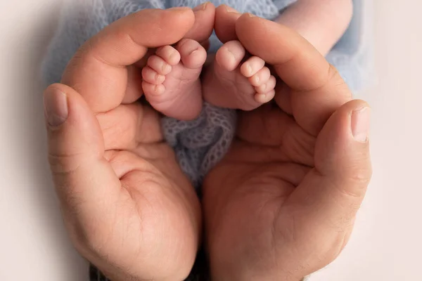 父亲的手掌，母亲用蓝色的毯子抱着新生儿的脚。新生儿的脚踏在父母的手掌上。小孩的脚趾、脚跟和脚的摄影. — 图库照片