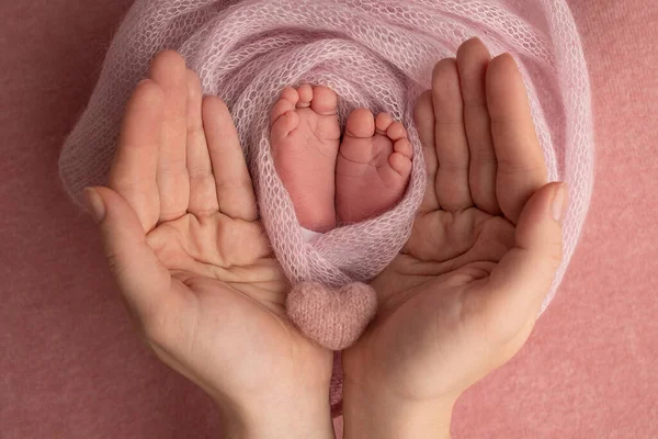 Babanın avuç içi, anne yeni doğan bebeğin ayağını pembe bir battaniyenin içinde tutuyor. Yeni doğan bebeğin ayakları, ebeveynlerin avuçlarında. Bir çocuğun ayak parmaklarının, topuklarının ve ayaklarının fotoğrafı. — Stok fotoğraf