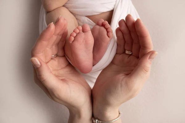 Ладони матери держат ногу новорожденного ребенка в белом одеяле. Ноги новорожденного на ладонях родителей. Studio macro photo of a child town, heels and foots. — стоковое фото