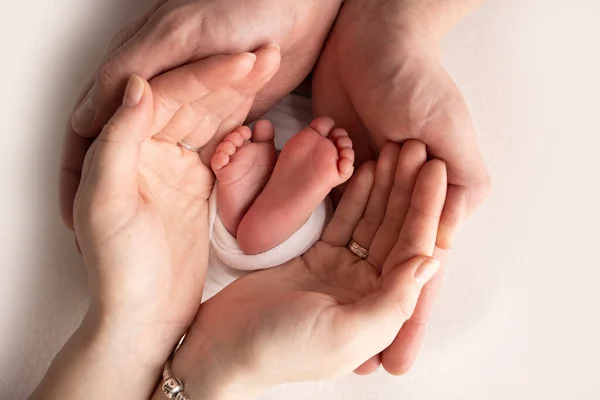 Annenin, babanın avuç içleri yeni doğan bebeğin ayağını beyaz bir battaniyenin içinde tutuyor. Yeni doğan bebeğin ayakları, ebeveynlerin avuçlarında. Stüdyo makro çocuk fotoğrafı. Parmak, topuklar ve ayaklar.. — Stok fotoğraf