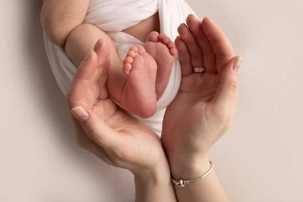 Annenin avuç içleri yeni doğan bebeğin ayağını beyaz bir battaniyenin içinde tutuyor. Yeni doğan bebeğin ayakları, ebeveynlerin avuçlarında. Stüdyo makro çocuk fotoğrafı. Parmak, topuklar ve ayaklar.. — Stok fotoğraf
