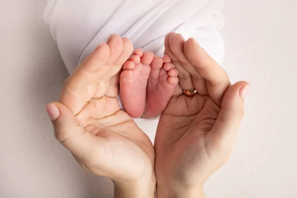 Annenin, babanın avuç içleri yeni doğan bebeğin ayağını beyaz arka planda tutuyor. Yeni doğan bebeğin ayakları, ebeveynlerin avuçlarında. Bir çocuğun ayak parmaklarının, topuklarının ve ayaklarının fotoğrafı. — Stok fotoğraf