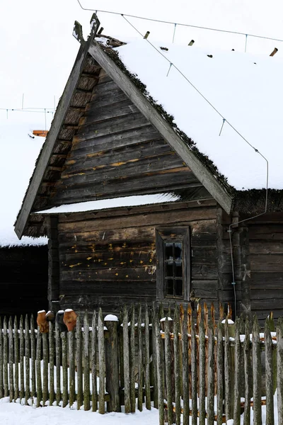 Старая деревянная хижина, бревенчатый дом с соломенной крышей. Заброшенная русская деревня, покрытая снегом. Бревенчатый дом с сараем с деревянным плетеным забором. — стоковое фото