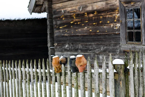 Inverno paisagem russa. Uma velha cabana de madeira, uma casa de madeira com um telhado de palha. Log house com um celeiro com uma cerca de vime de madeira e vasos de barro. — Fotografia de Stock