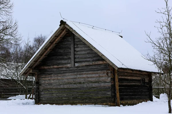 Inverno paisagem russa. Uma velha cabana de madeira, uma casa de madeira com um telhado de palha. Aldeia russa abandonada coberta de neve. Casa de madeira com celeiro. — Fotografia de Stock