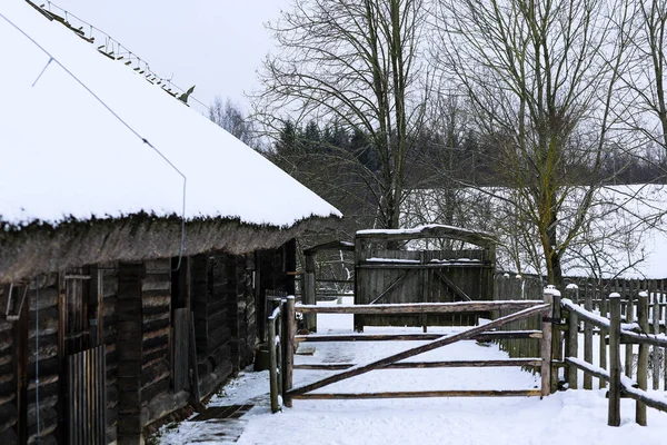 Paysage russe d'hiver. Une vieille cabane en bois, une maison en rondins avec un toit de chaume. Village russe abandonné couvert de neige. Maison en bois rond avec une grange avec une clôture en osier en bois. — Photo