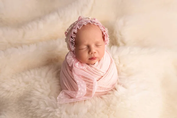 Спящая новорожденная девочка в первые дни жизни в розовом коконе с розовой кепкой на белом фоне. Студийная макрофотография, портрет новорожденного ребенка. Понятие женского счастья. — стоковое фото