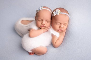 Yeni doğmuş küçük ikiz kızlar. Yeni doğmuş bir ikiz, beyaz bandajlı ve beyaz yünlü elbiseli soluk mavi bir battaniyeye karşı kız kardeşinin üzerine sarılıp uyur..