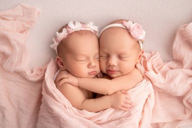 Yeni doğmuş küçük ikiz kızlar. Yeni doğmuş bir ikiz, kız kardeşinin yanında uyur. Pembe bandajlı pembe bir battaniyenin arkasında yeni doğmuş ikiz kızlar. Kızlar nazikçe sarılıp kız kardeşlerini öpüyor..