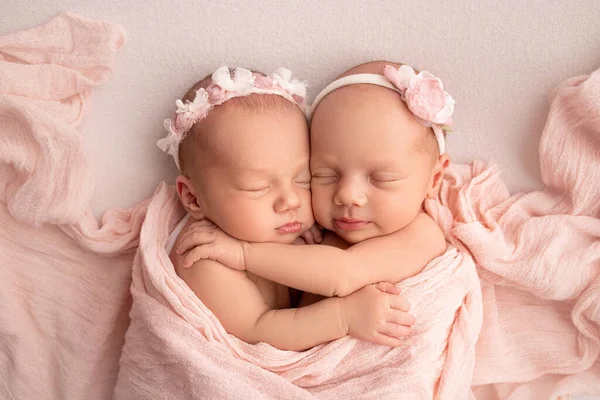 Крихітні новонароджені дівчата-близнюки. Новий близнюк спить поруч з сестрою. Новонароджені дівчата-близнюки на тлі рожевої ковдри з рожевими бинтами. Дівчата ніжно обіймають і цілують свою сестру в милій позі . — стокове фото
