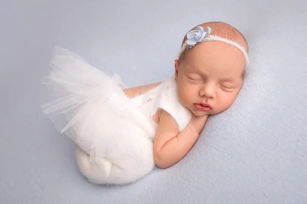 Niña recién nacida dormida en los primeros días de vida en un vestido de ballet blanco con una venda blanca y una flor azul sobre un fondo azul. Estudio macrofotografía, retrato de una bailarina recién nacida. — Foto de Stock