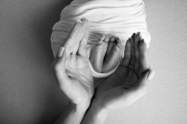 The palms of the father, the mother are holding the foot of the newborn baby. Feet of the newborn on the palms of the parents. Photography of a childs toes, heels and feet. Black and white photo. — Stock Photo, Image