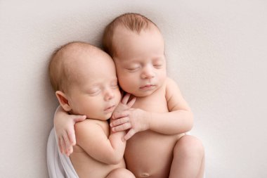 Tiny newborn twins boys in white cocoons on a white background. A newborn twin sleeps next to his brother. Newborn two twins boys hugging each other.Professional studio photography