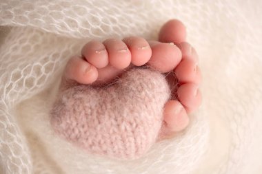 The tiny foot of a newborn baby. Soft feet of a new born in a purple, lilac wool blanket. Close up of toes, heels and feet of a newborn. Knitted purple, lilac heart in the legs of a baby. 