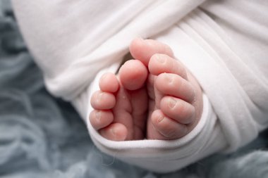 The tiny foot of a newborn. Soft feet of a newborn in a white blanket and on a blue background. Close up of toes, heels and feet of a newborn baby. Studio Macro photography. Womans happiness