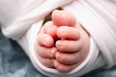 The tiny foot of a newborn. Soft feet of a newborn in a white blanket and on a blue background. Close up of toes, heels and feet of a newborn baby. Studio Macro photography. Womans happiness. 