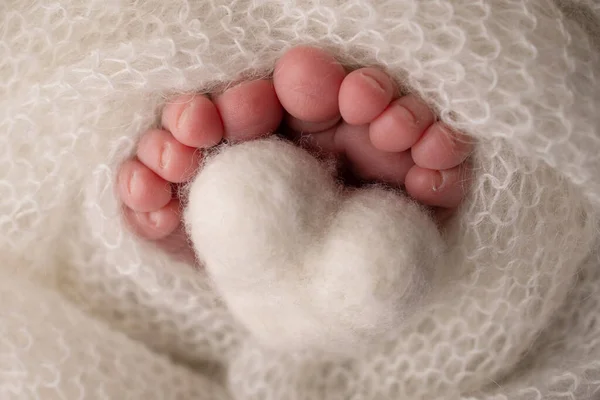 Close-up of a newborn babys tiny feet wrapped in a knitted white wool blanket with a small felt heart.