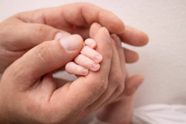 A newborn holds on to moms, dads finger. Hands of parents and baby close up. A child trusts and holds her tight. Tiny fingers of a newborn. The family is holding hands. Concepts of family and love. 