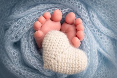 Yeni doğmuş bir bebeğin küçük ayağı. Beyaz yün battaniyenin içinde yeni doğmuş bir bebeğin yumuşak ayakları. Ayak parmakları, topuklar ve yeni doğmuş bir bebeğin ayakları. Bir bebeğin bacaklarında örülmüş beyaz kalp. Makro fotoğrafçılık. 