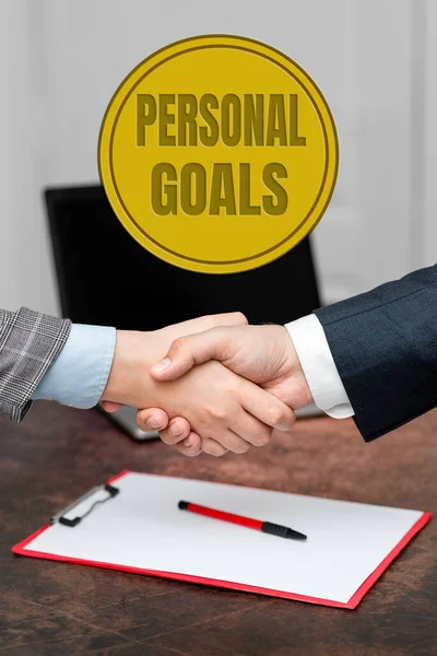 Hand writing sign Personal Goals. Word Written on Target set by a person to influence his efforts Motivation Two Professional Well-Dressed Corporate Businessmen Handshake Indoors