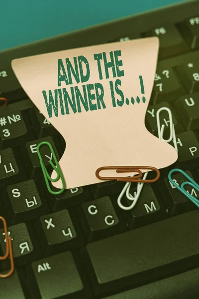 Handwriting text And The Winner Is. Business approach announcing who got first place at competition or exam Multiple Assorted Collection Office Stationery Photo Placed Over Table — Stock Photo, Image